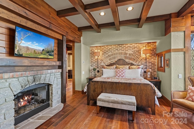 bedroom with a stone fireplace, coffered ceiling, hardwood / wood-style floors, and beam ceiling