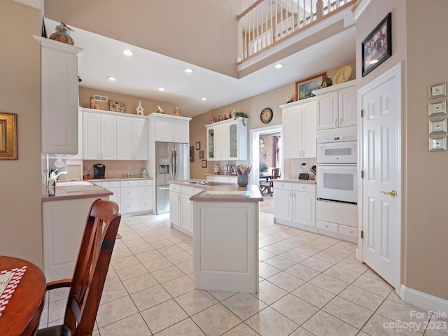 kitchen featuring a towering ceiling, white cabinetry, light tile patterned floors, a center island, and double oven