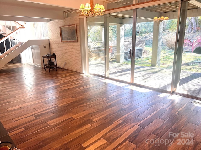 unfurnished living room featuring an inviting chandelier, brick wall, and dark wood-type flooring