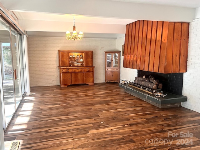 unfurnished living room with a notable chandelier, brick wall, and dark wood-type flooring