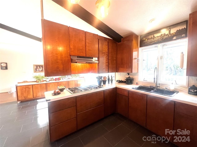 kitchen with kitchen peninsula, lofted ceiling, dark tile flooring, stainless steel gas cooktop, and sink