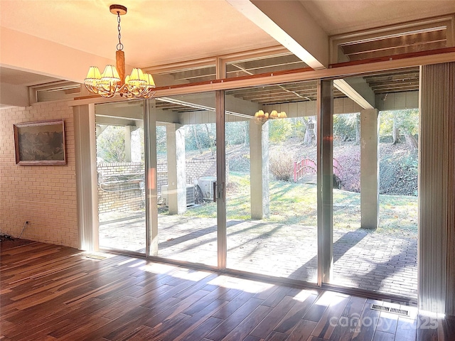 doorway to outside featuring floor to ceiling windows, brick wall, dark wood-type flooring, and an inviting chandelier