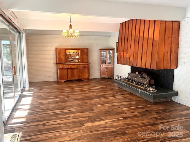 interior space featuring brick wall, dark wood finished floors, visible vents, and an inviting chandelier