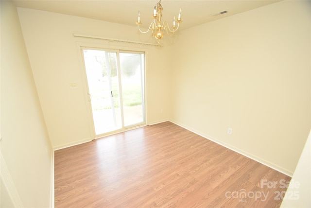 spare room with light wood-type flooring and an inviting chandelier