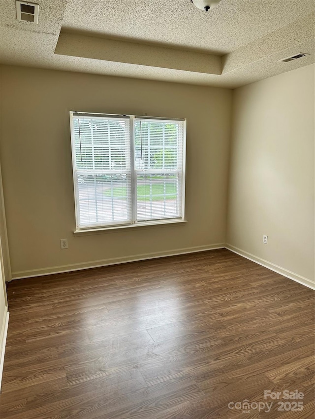 unfurnished room with dark hardwood / wood-style flooring, a raised ceiling, and a textured ceiling