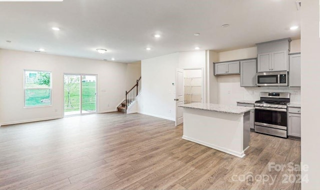 kitchen featuring light stone countertops, gray cabinetry, stainless steel appliances, light hardwood / wood-style floors, and a kitchen island