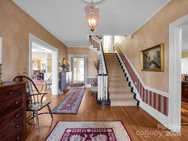 entryway with wood-type flooring, a notable chandelier, and ornamental molding