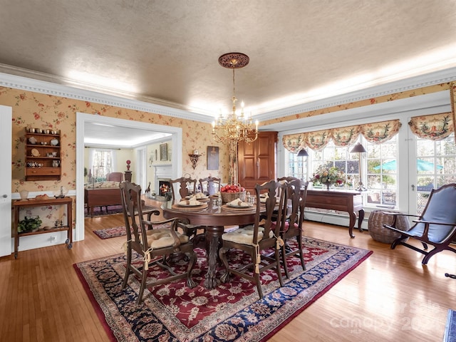 dining area with a textured ceiling, an inviting chandelier, light hardwood / wood-style flooring, crown molding, and baseboard heating