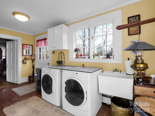 clothes washing area featuring cabinets, ornamental molding, sink, washing machine and dryer, and baseboard heating