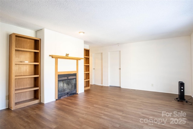 unfurnished living room with built in shelves, a textured ceiling, and dark wood-type flooring