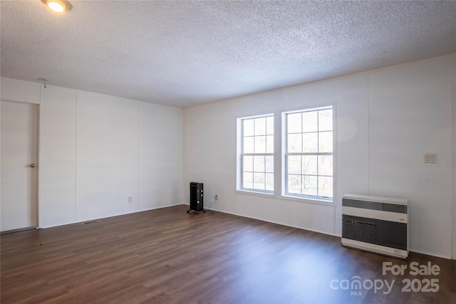 unfurnished room with dark hardwood / wood-style flooring, a textured ceiling, and heating unit