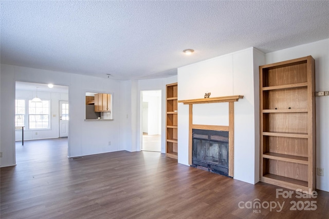 unfurnished living room featuring built in shelves, dark wood-type flooring, and a textured ceiling