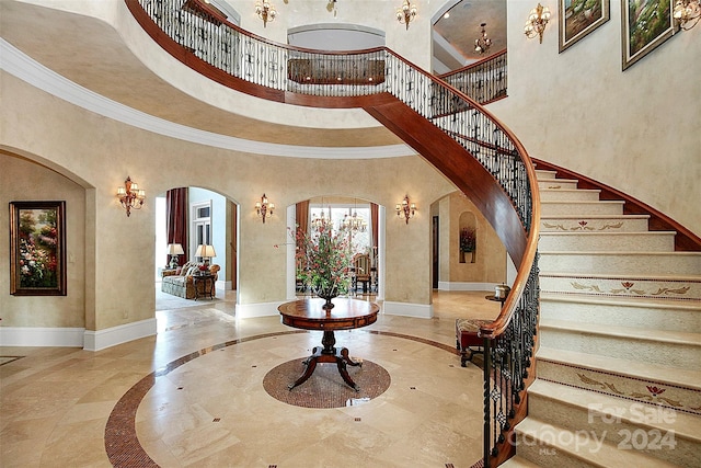 interior space with a towering ceiling, crown molding, and light tile flooring