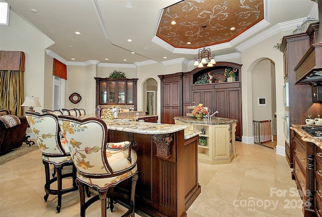 kitchen featuring light tile floors, a center island with sink, a tray ceiling, and an inviting chandelier