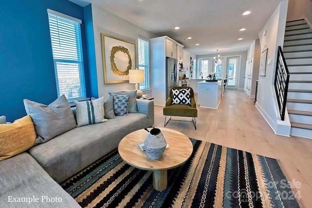 living room with an inviting chandelier, sink, light wood-type flooring, and a healthy amount of sunlight