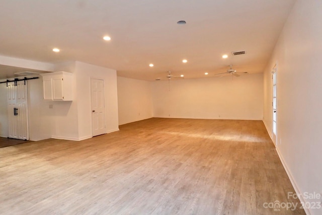 empty room with a barn door, light hardwood / wood-style floors, and ceiling fan