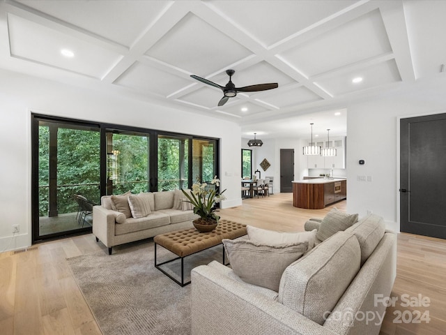 living room featuring a healthy amount of sunlight, light hardwood / wood-style flooring, coffered ceiling, and ceiling fan