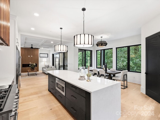 kitchen with stainless steel microwave, decorative light fixtures, light hardwood / wood-style floors, a center island, and coffered ceiling