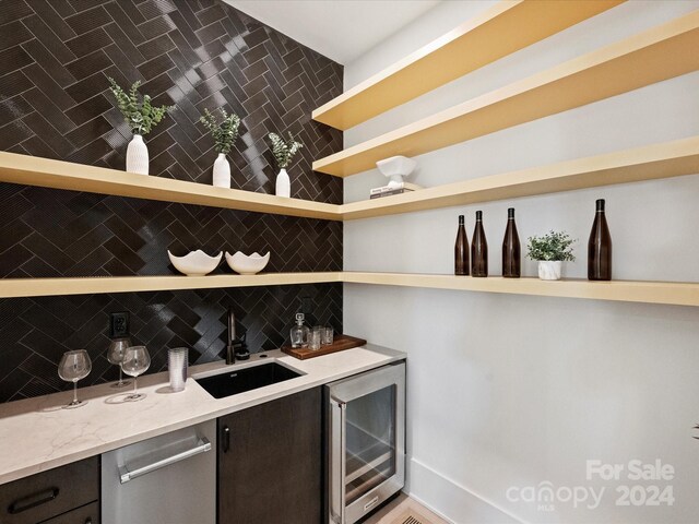 bar with beverage cooler, decorative backsplash, sink, light stone countertops, and dark brown cabinetry