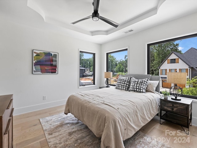 bedroom with ceiling fan, multiple windows, a tray ceiling, and light hardwood / wood-style floors