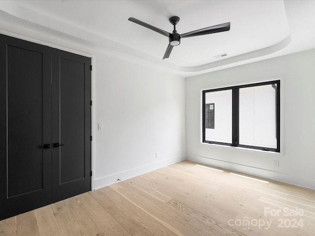 interior space with ceiling fan, light wood-type flooring, and a tray ceiling