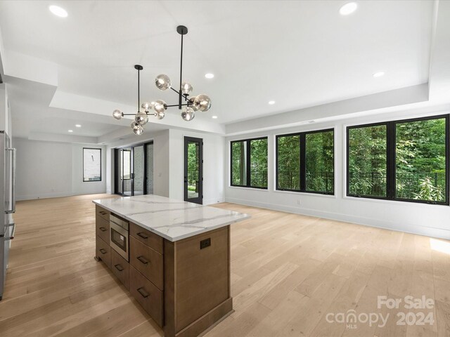 kitchen with hanging light fixtures, light hardwood / wood-style flooring, a healthy amount of sunlight, and a tray ceiling