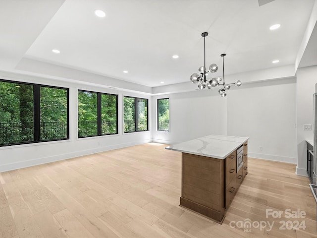 kitchen with pendant lighting, light wood-type flooring, light stone countertops, a center island, and a notable chandelier