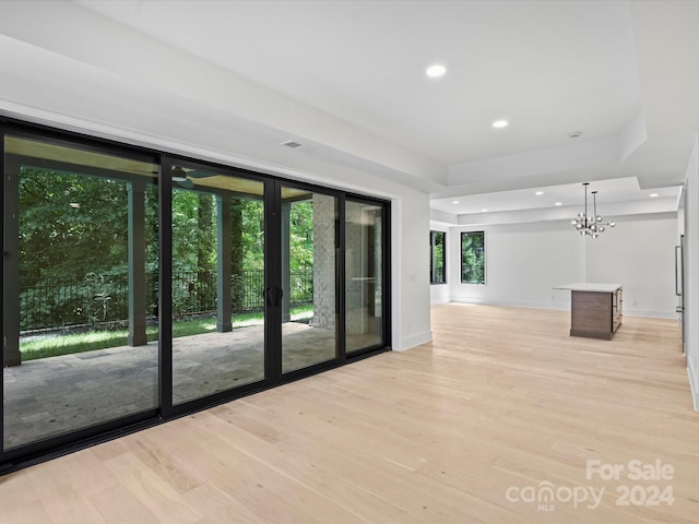 unfurnished room with a notable chandelier, light hardwood / wood-style flooring, and a raised ceiling