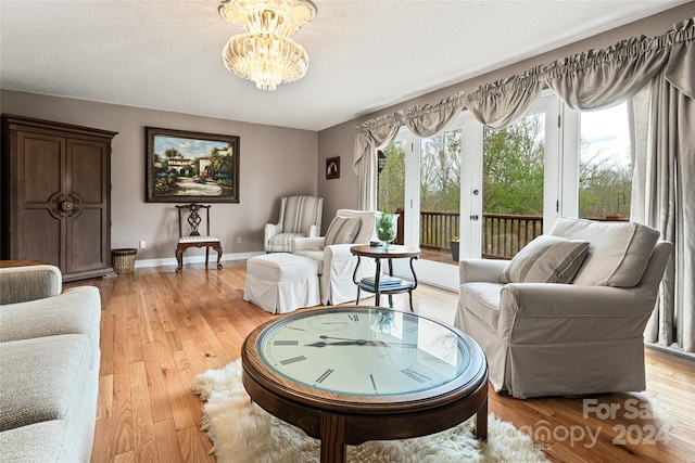 living room featuring a textured ceiling, a notable chandelier, french doors, and light hardwood / wood-style floors