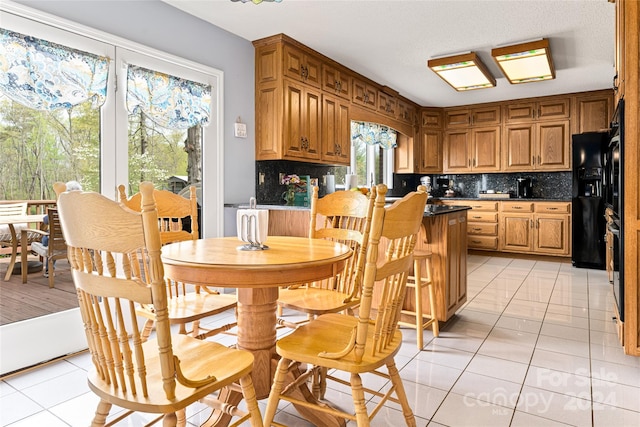 interior space with black fridge, light tile patterned floors, and decorative backsplash