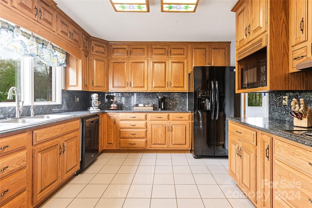 kitchen featuring dark stone countertops, tasteful backsplash, light tile patterned floors, black appliances, and sink