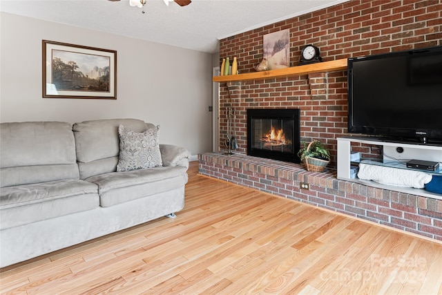 living room featuring a brick fireplace, light hardwood / wood-style floors, brick wall, ceiling fan, and a textured ceiling