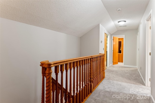 hall with lofted ceiling, carpet, and a textured ceiling