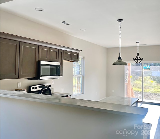 kitchen featuring decorative light fixtures, a healthy amount of sunlight, dark brown cabinetry, and range