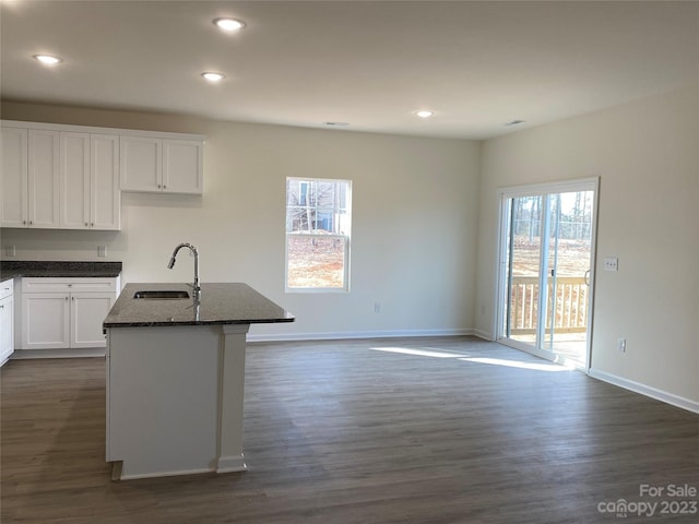 kitchen featuring dark stone counters, sink, white cabinetry, and a center island with sink