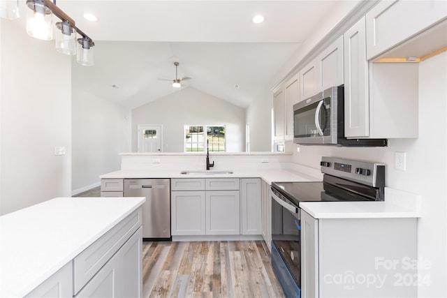 kitchen with light hardwood / wood-style floors, appliances with stainless steel finishes, sink, decorative light fixtures, and lofted ceiling