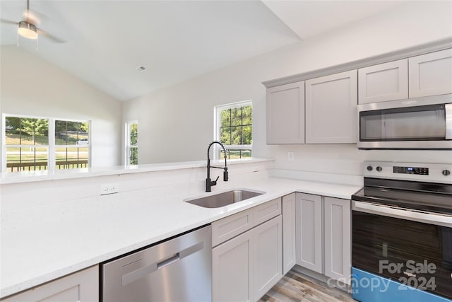 kitchen with vaulted ceiling, stainless steel appliances, sink, gray cabinets, and light wood-type flooring