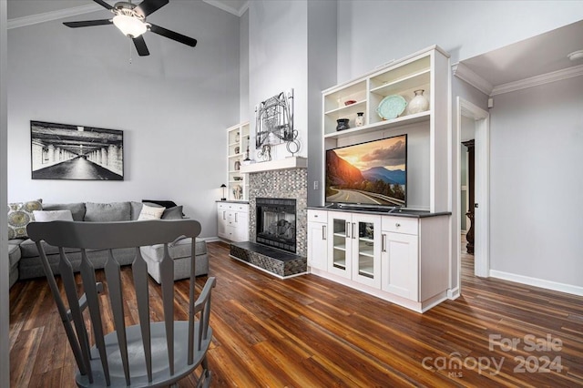 living room featuring ceiling fan, dark hardwood / wood-style floors, a tile fireplace, and ornamental molding