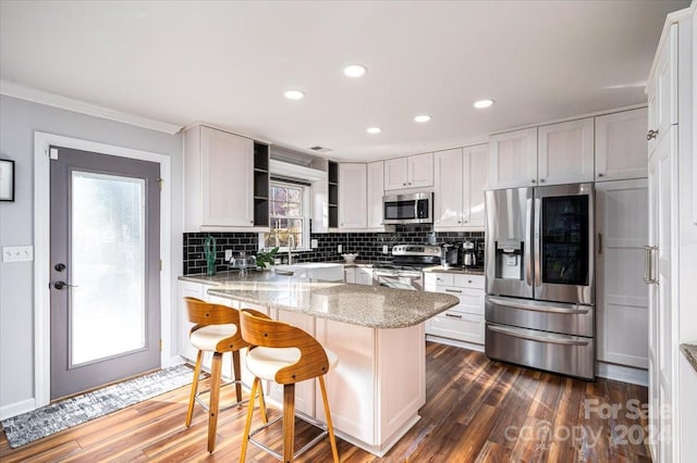 kitchen with appliances with stainless steel finishes, white cabinetry, light stone countertops, a healthy amount of sunlight, and a breakfast bar