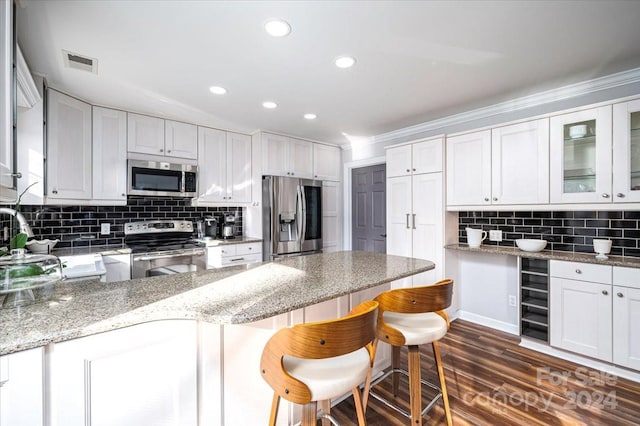 kitchen with appliances with stainless steel finishes, dark wood-type flooring, white cabinetry, light stone counters, and a kitchen bar