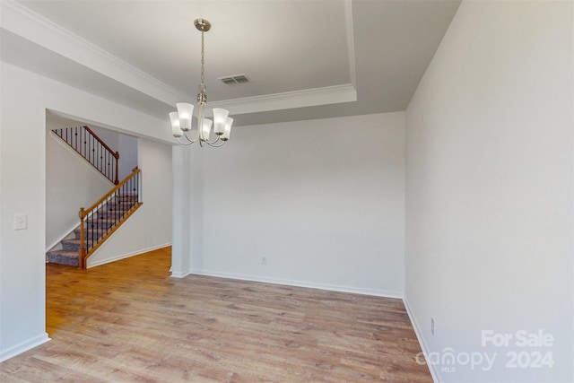 empty room with ornamental molding, a raised ceiling, a chandelier, and light hardwood / wood-style floors