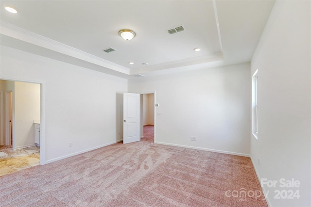 unfurnished bedroom featuring light carpet, ensuite bath, and a tray ceiling