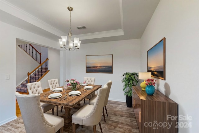 dining space featuring a notable chandelier, a raised ceiling, crown molding, and hardwood / wood-style floors