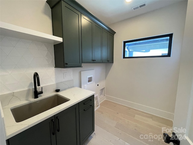 kitchen with backsplash, light stone counters, light wood-type flooring, and sink