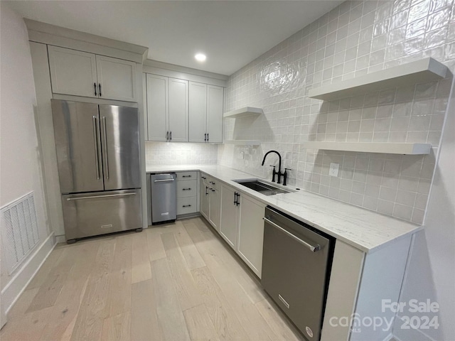 kitchen with decorative backsplash, appliances with stainless steel finishes, light stone counters, sink, and light hardwood / wood-style floors