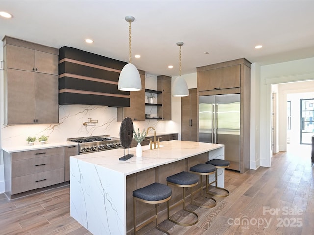 kitchen featuring a breakfast bar area, a center island with sink, high quality appliances, custom range hood, and light hardwood / wood-style floors