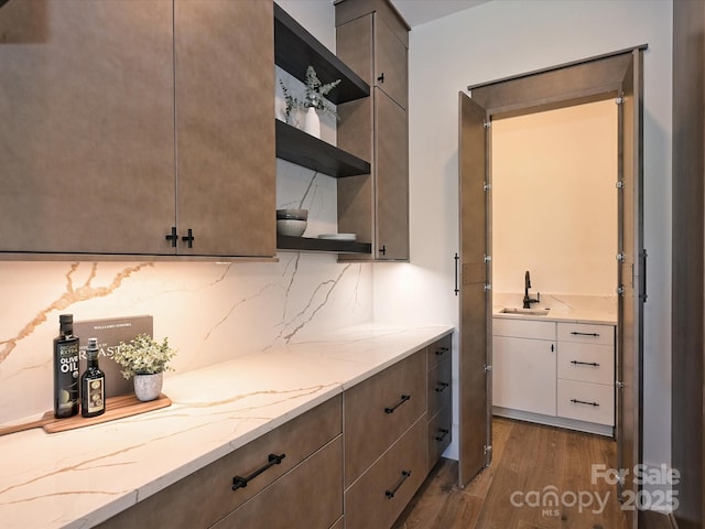 kitchen with dark wood-type flooring, light stone countertops, sink, and decorative backsplash