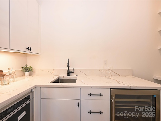 kitchen with white cabinetry, sink, dishwashing machine, beverage cooler, and light stone countertops