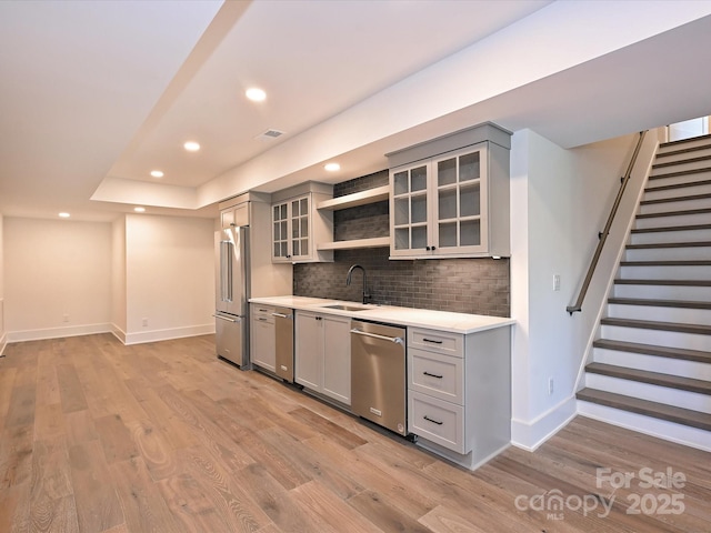 kitchen with gray cabinets, sink, decorative backsplash, stainless steel appliances, and light hardwood / wood-style flooring