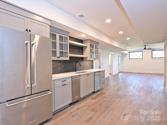 kitchen with gray cabinets, appliances with stainless steel finishes, sink, decorative backsplash, and light wood-type flooring